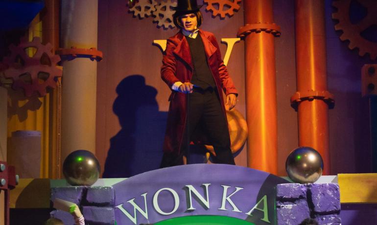 People in Willy Wonka costumes on a colorful stage.