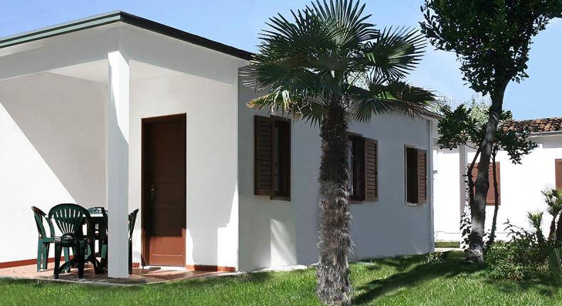 Bungalow blanc avec palmiers et chaises vertes à l'extérieur.